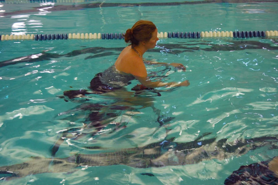 Femme pédalant sur un aquabike immergée jusqu'à la poitrine dans une piscine couverte