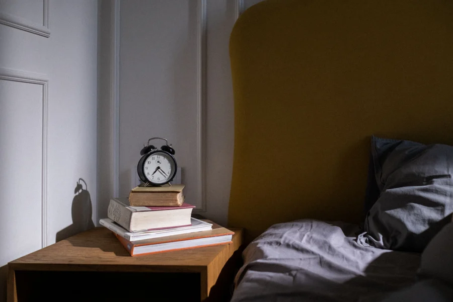 Réveil posé sur une pile de livres, sur une table de chevet près d’un lit