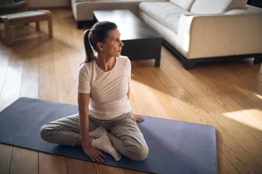 Femme assise sur un tapis de yoga dans un salon lumineux, en légère torsion